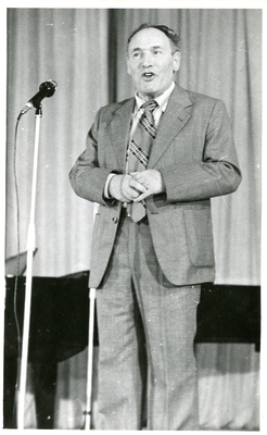 Фотопортрет Пресмана Г., поколенный, анфас, руки почти на груди. Стоит перед микрофоном  у рояля.