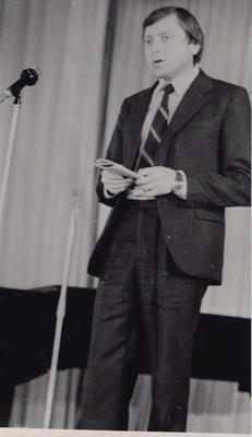 Фотопортрет Лисняка А.А., поколенный, 3/4, в руках книга. Стоит перед микрофоном  у рояля.