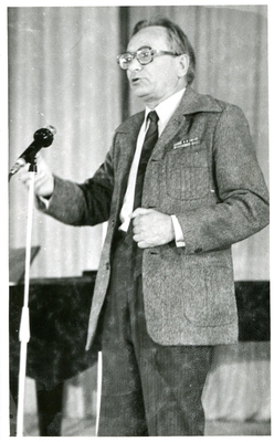 Фотопортрет Полякова В., поколенный, 3/4, в очках. Стоит перед микрофоном  у рояля.