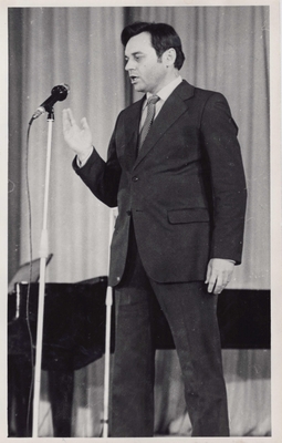 Фотопортрет Голубева А.А., поколенный, профиль, одна рука согнута в локте. Стоит перед микрофоном  у рояля.